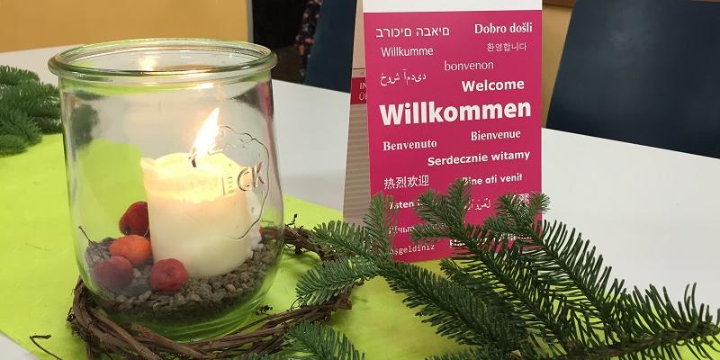 Willkommensgruß in vielen Sprachen mit Tannenzweig und Kerze